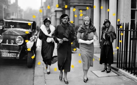 Vier Frauen in eleganter 30er Jahre Mode, Pelzmänteln und Hüten spazieren an einem Oldtimer entlang.
