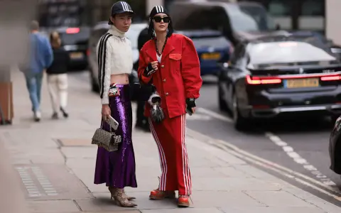 Zwei Personen präsentieren ihren **new money style** auf der Straße: glitzernder lila Rock, rote Jacke und sportliche Elemente.