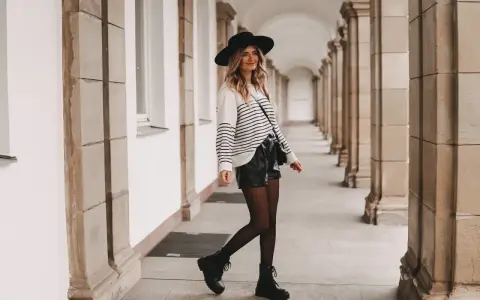 Frau mit Hut und gestreiftem Pullover, die stylische ledershorts kombinieren. Schwarze Stiefel und Strumpfhose runden den Look ab.