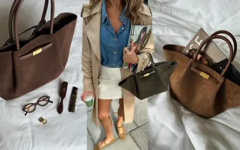 Braune Wildleder Demellier New York Tote mit goldenem Verschluss, daneben Brille, Ringe und Bürsten.