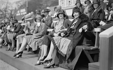 Frauen in eleganten Hüten und Kleidern, ein Bild der Weimarer Republik Mode, sitzen auf einer Tribüne.