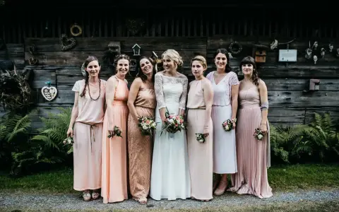 Brautjungfern in zarten Pastelltönen posieren vor rustikaler Holzwand, ein Bild von einer entspannten boho hochzeit.