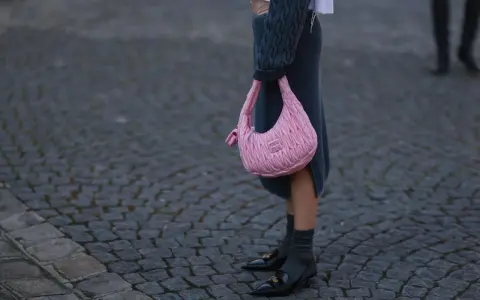 Ein grauer Strickrock kombiniert mit einem Oversize-Pullover und einer pinken Tasche.