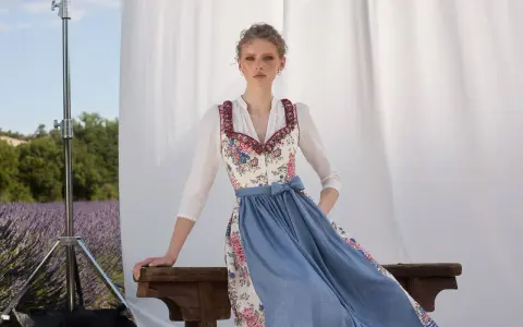 Ein Dirndl im floralen Muster mit blauem Rock, ein moderner Dirndl-Trend, posiert vor Lavendelfeld-Kulisse.