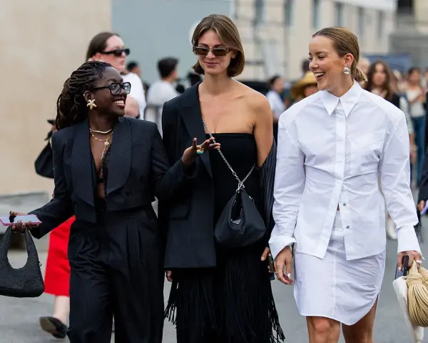 Drei Frauen präsentieren unterschiedliche, modische clothing styles: ein schwarzer Anzug, ein schwarzes Kleid mit Fransen und ein weißes Hemd mit Rock.