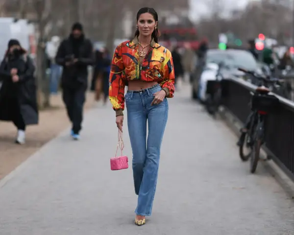 Stylische Frau in bunten Jackett und bootcut jeans kombinieren mit pinker Tasche und auffälligen Schuhen.