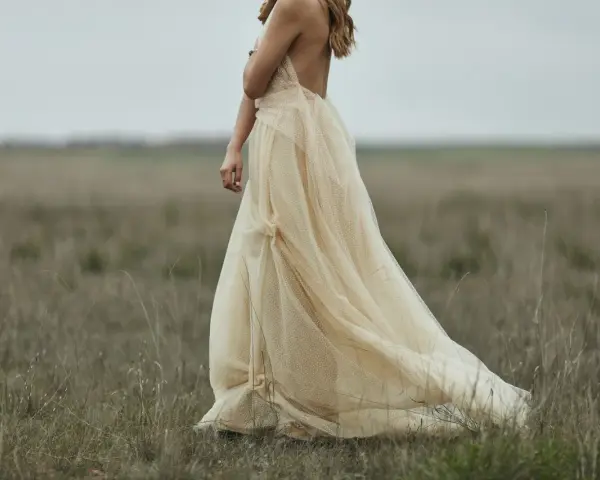 Braut in einem fließenden, cremefarbenen Kleid mit Tupfenmuster, das perfekt zum **dresscode boho hochzeit** passt. Sie steht in einer weiten, grasbewachsenen Ebene.