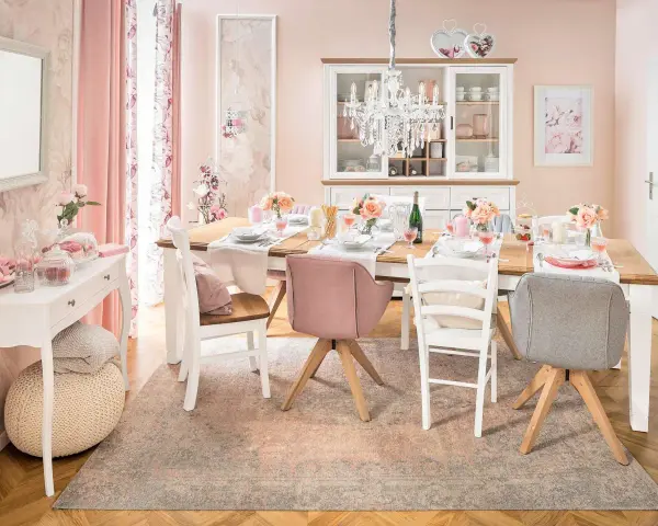 Ein Esstisch im Cottagecore-Stil, gedeckt mit Blumen und rosafarbenen Akzenten. Ein Kronleuchter hängt über dem Tisch.