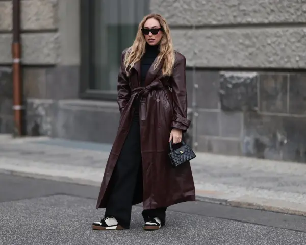 Frau in braunem Leder-Trenchcoat und schwarzen Hosen. Die Frage, welche Farbe passt zu schwarz, wird hier elegant beantwortet: Braun und Schwarz sind ein tolles Duo.