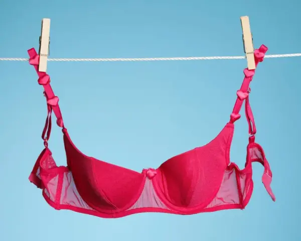 Ein roter BH mit Herzchen-Trägern hängt an einer Wäscheleine. Frisch gewaschen und bereit zum Trocknen.