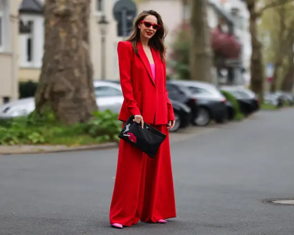 Frau in rotem Hosenanzug mit pinkem Top und Clutch mit Lippenmotiv. Was passt zu roter Hose? Dieser Look zeigt es!