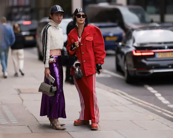 Zwei Personen präsentieren ihren **new money style** auf der Straße: glitzernder lila Rock, rote Jacke und sportliche Elemente.
