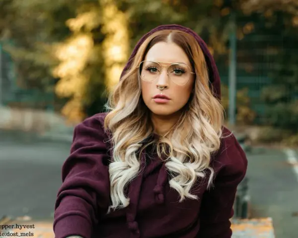 Frau mit blonden Haaren und Brille trägt einen Kapuzenpullover in dunklem Beere. Die Farbe Beere kombiniert sie gekonnt mit ihrem Outfit.