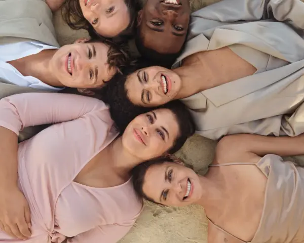 Sechs lächelnde Menschen liegen eng beieinander. Ihre Kleidung, wie ein beiger Anzug und ein rosafarbenes Kleid, inspiriert die Idee einer leichten basisgarderobe sommertyp.