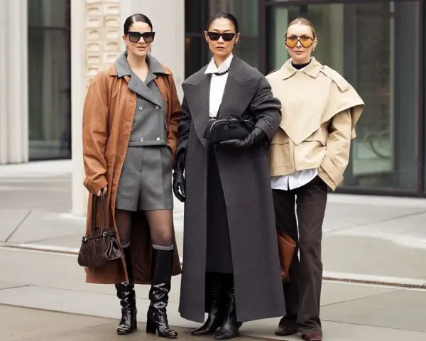 Drei Frauen präsentieren stilvolle Outfits im layering look: brauner Mantel über grauem Anzug, langer grauer Mantel und beiger Kurzmantel über weißem Hemd.