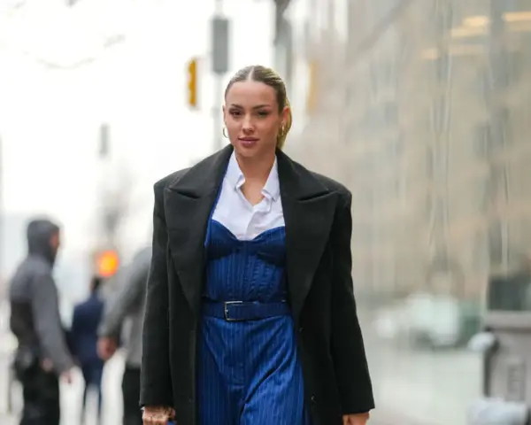Frau trägt eine schwarze Jacke über einem blauen Nadelstreifen-Jumpsuit mit Korsett-Oberteil und weißem Hemd.