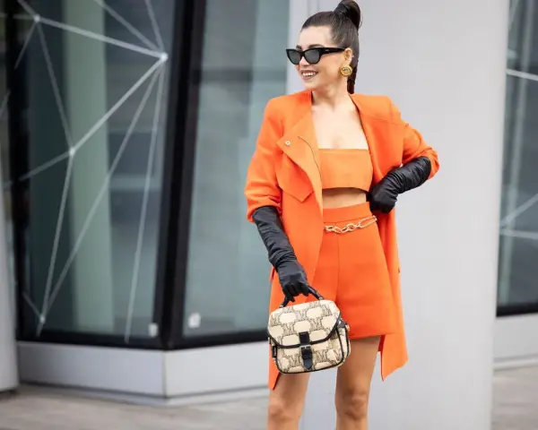 Eine Frau in einem leuchtend orangen Outfit mit schwarzen Handschuhen und einer Tasche. Schwarz passt wunderbar zu Orange, eine tolle Farbkombination!