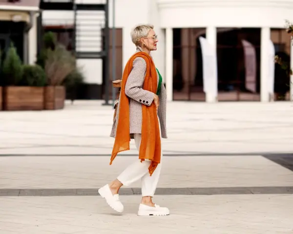 Coole Frauen mit 50: Stilvoll in kariertem Blazer, orangefarbenem Schal und weißen Hosen.