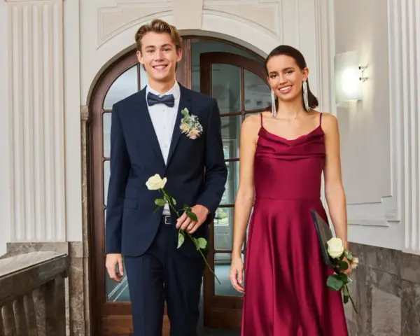 Elegantes Outfit für einen Jugendweihe Gast: Ein junger Mann im dunkelblauen Anzug mit Fliege und eine Frau im weinroten Kleid.