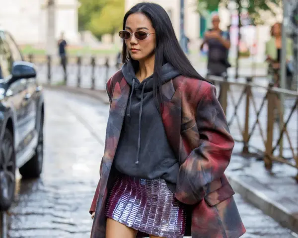 Frau in stylischem Outfit mit pailletten hose, Hoodie und gemustertem Blazer.