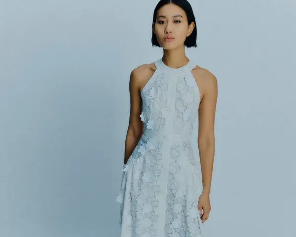 Ein Model trägt ein weißes Spitzenkleid mit Blumenapplikationen. Welche Farbe passt zu Himmelblau? Dieses Kleid ist eine zarte Antwort.
