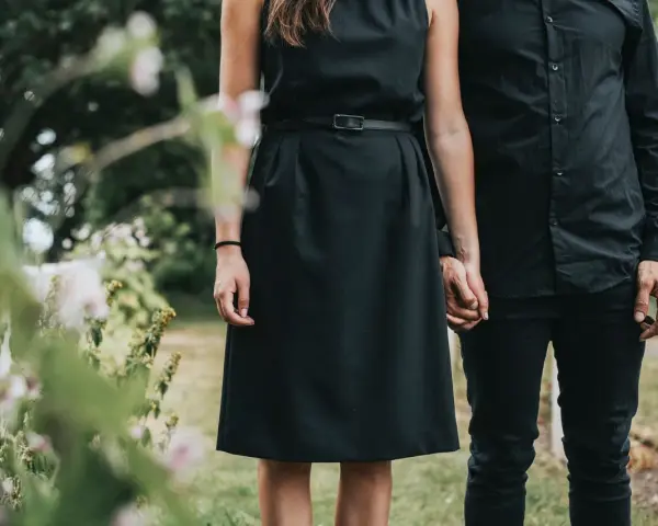 Frau in schwarzem Kleid und Mann in schwarzer Kleidung halten Händchen. So zieht man zur Beerdigung an als Frau.