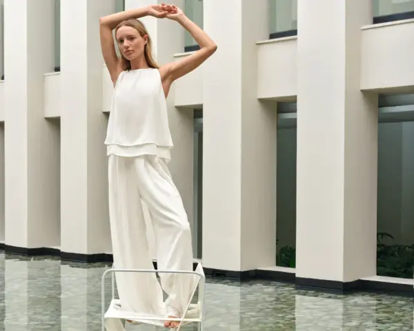 Frau in weißem Outfit mit weiten Palazzo Hosen, elegant gestylt vor moderner Architektur.