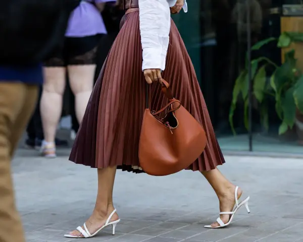 Elegant brauner Faltenrock, kombiniert mit weißer Bluse und cognacfarbener Tasche. Ein stilvoller Look für den Sommer.