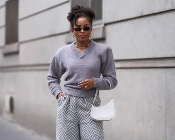 Eine Frau in grauem Pullover und Hose mit Zickzackmuster. Sie trägt eine weiße Tasche. Ein Beispiel, welche Farben passen zu grau.