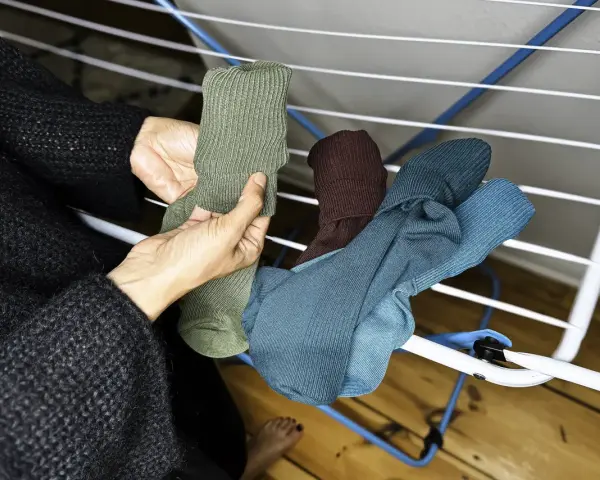 Hände sortieren frisch gewaschene, bunte Socken auf einem Wäscheständer.