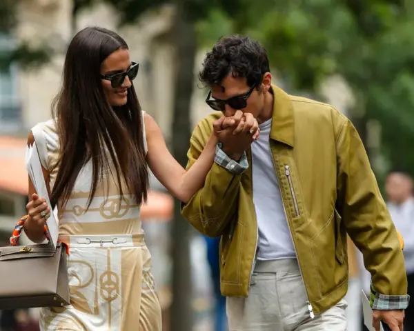 Ein Mann küsst die Hand einer Frau. Ihr **outfit erstes date** ist elegant: Sie trägt ein gemustertes Kleid, er eine olivgrüne Jacke.