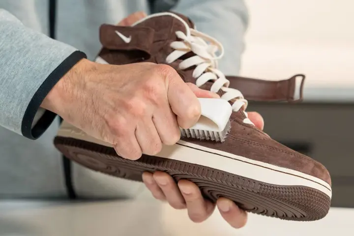 Hände reinigen braune Wildleder Schuhe mit einer Bürste. So werden die Lieblingssneaker wieder wie neu.