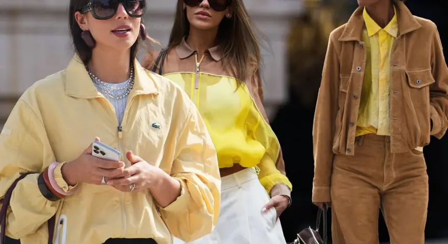 Drei Frauen in modischen Outfits. Die vordere trägt eine gelbe Jacke, die mittlere ein gelbes Top. Welche Farbe passt zu Gelb? Braun, wie die Jacke der rechten Frau, ist eine tolle Wahl.