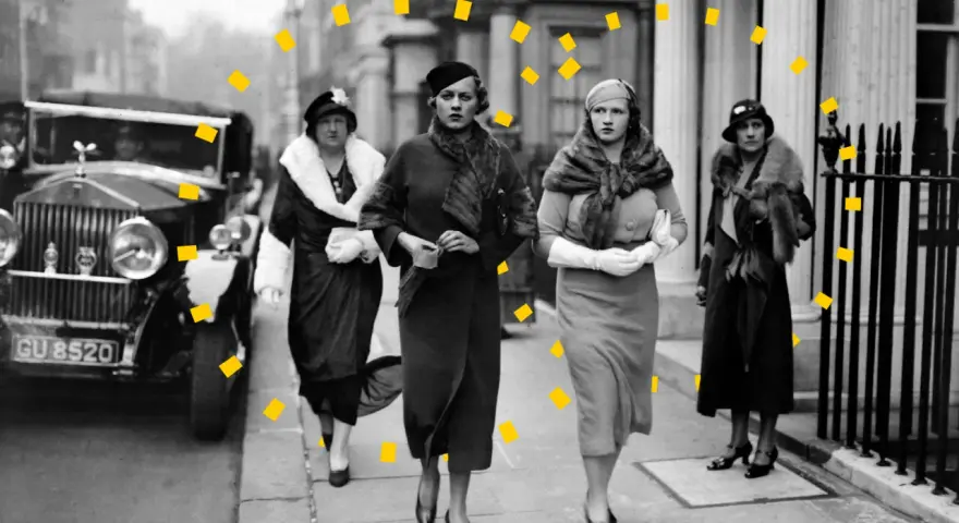 Vier Frauen in eleganter 30er Jahre Mode, Pelzmänteln und Hüten spazieren an einem Oldtimer entlang.
