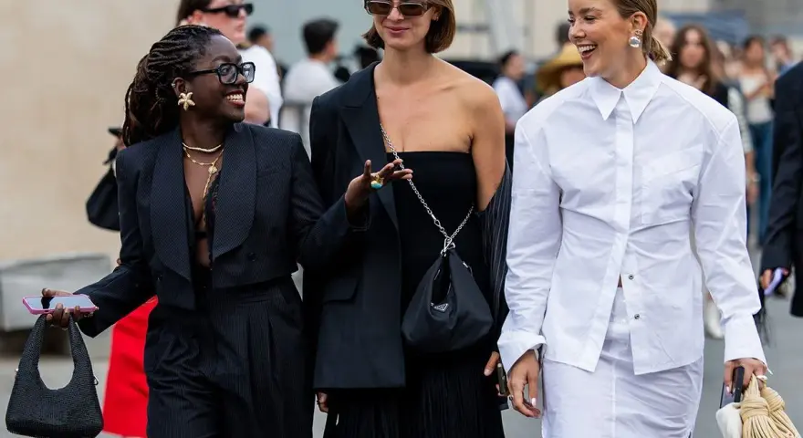 Drei Frauen präsentieren unterschiedliche, modische clothing styles: ein schwarzer Anzug, ein schwarzes Kleid mit Fransen und ein weißes Hemd mit Rock.
