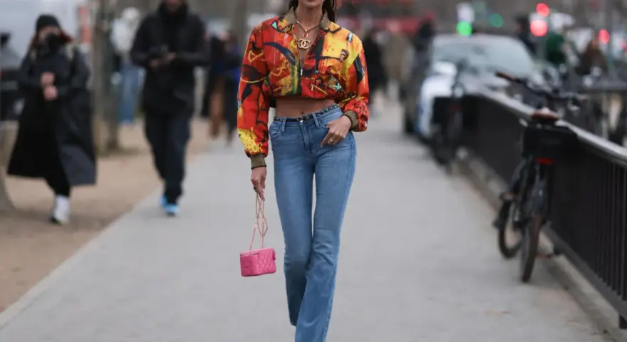 Stylische Frau in bunten Jackett und bootcut jeans kombinieren mit pinker Tasche und auffälligen Schuhen.