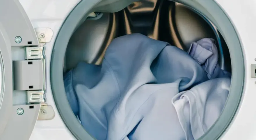 Blaue Wäsche in einer offenen Waschmaschine. Die Frage, ob Polyester einlaufen kann, beschäftigt viele.