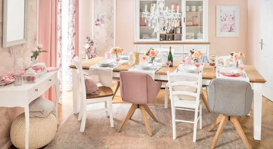 Ein Esstisch im Cottagecore-Stil, gedeckt mit Blumen und rosafarbenen Akzenten. Ein Kronleuchter hängt über dem Tisch.