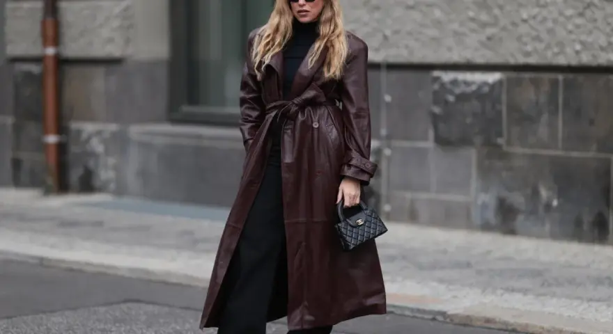 Frau in braunem Leder-Trenchcoat und schwarzen Hosen. Die Frage, welche Farbe passt zu schwarz, wird hier elegant beantwortet: Braun und Schwarz sind ein tolles Duo.