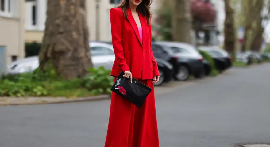 Frau in rotem Hosenanzug mit pinkem Top und Clutch mit Lippenmotiv. Was passt zu roter Hose? Dieser Look zeigt es!