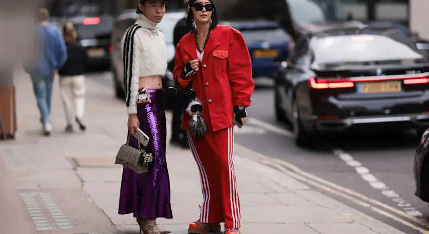 Zwei Personen präsentieren ihren **new money style** auf der Straße: glitzernder lila Rock, rote Jacke und sportliche Elemente.