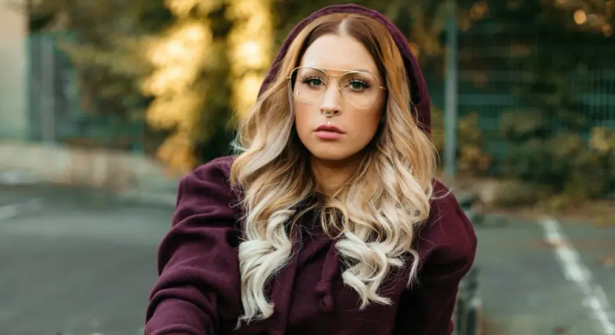 Frau mit blonden Haaren und Brille trägt einen Kapuzenpullover in dunklem Beere. Die Farbe Beere kombiniert sie gekonnt mit ihrem Outfit.
