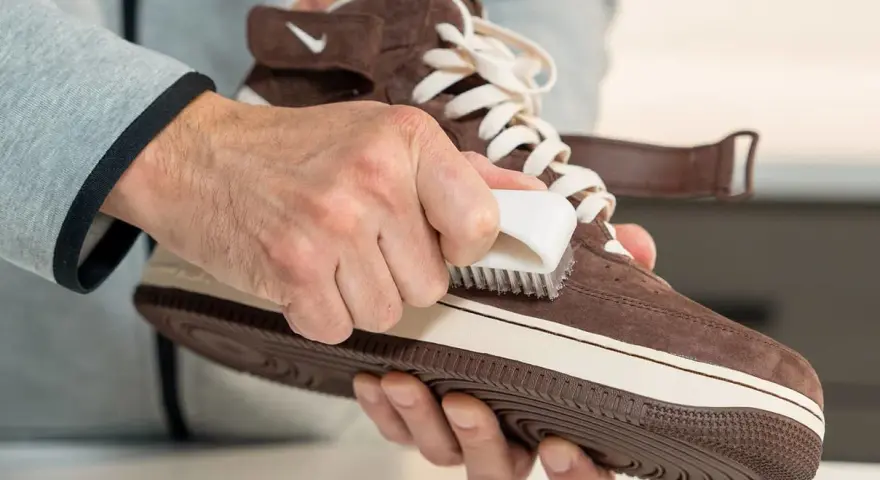 Hände reinigen braune Wildleder Schuhe mit einer Bürste. So werden die Lieblingssneaker wieder wie neu.