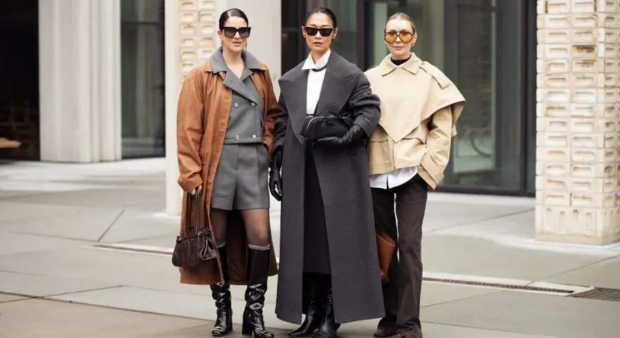 Drei Frauen präsentieren stilvolle Outfits im layering look: brauner Mantel über grauem Anzug, langer grauer Mantel und beiger Kurzmantel über weißem Hemd.