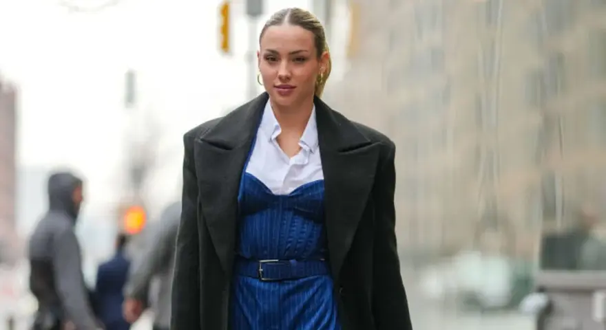 Frau trägt eine schwarze Jacke über einem blauen Nadelstreifen-Jumpsuit mit Korsett-Oberteil und weißem Hemd.