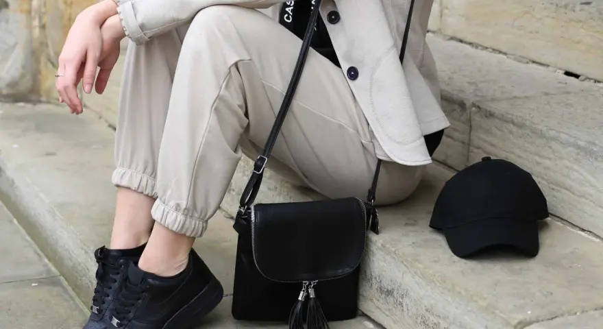 Stylisches flugzeug outfit damen: beige Hose, Blazer, schwarze Sneaker, Tasche und Cap. Perfekt für die Reise.