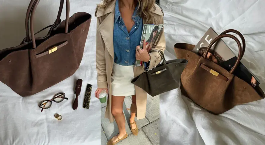 Braune Wildleder Demellier New York Tote mit goldenem Verschluss, daneben Brille, Ringe und Bürsten.