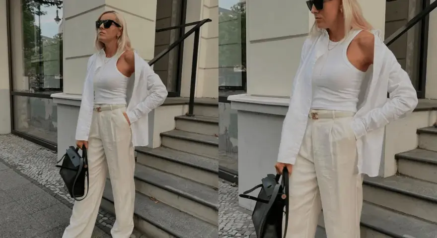 Eine Frau im Stil von quiet luxury, gekleidet in weiße Kleidung, steht vor einer Treppe.