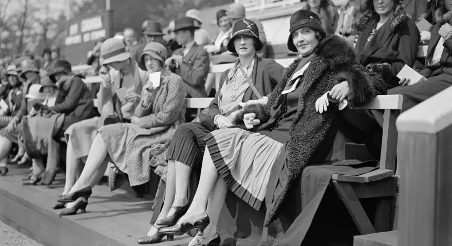 Frauen in eleganten Hüten und Kleidern, ein Bild der Weimarer Republik Mode, sitzen auf einer Tribüne.