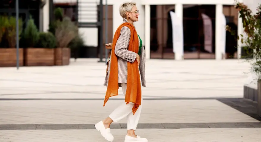Coole Frauen mit 50: Stilvoll in kariertem Blazer, orangefarbenem Schal und weißen Hosen.